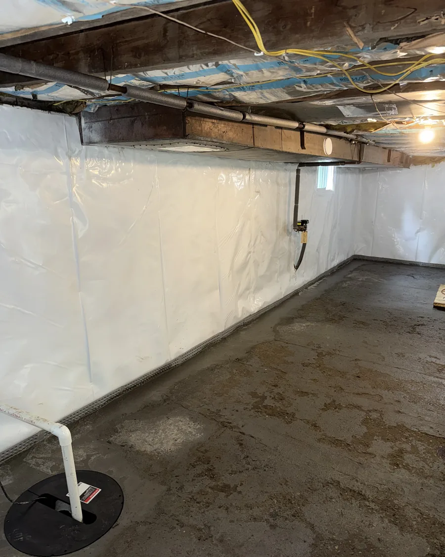 Basement with wall vapor barrier installed and a sump basin set into the floor