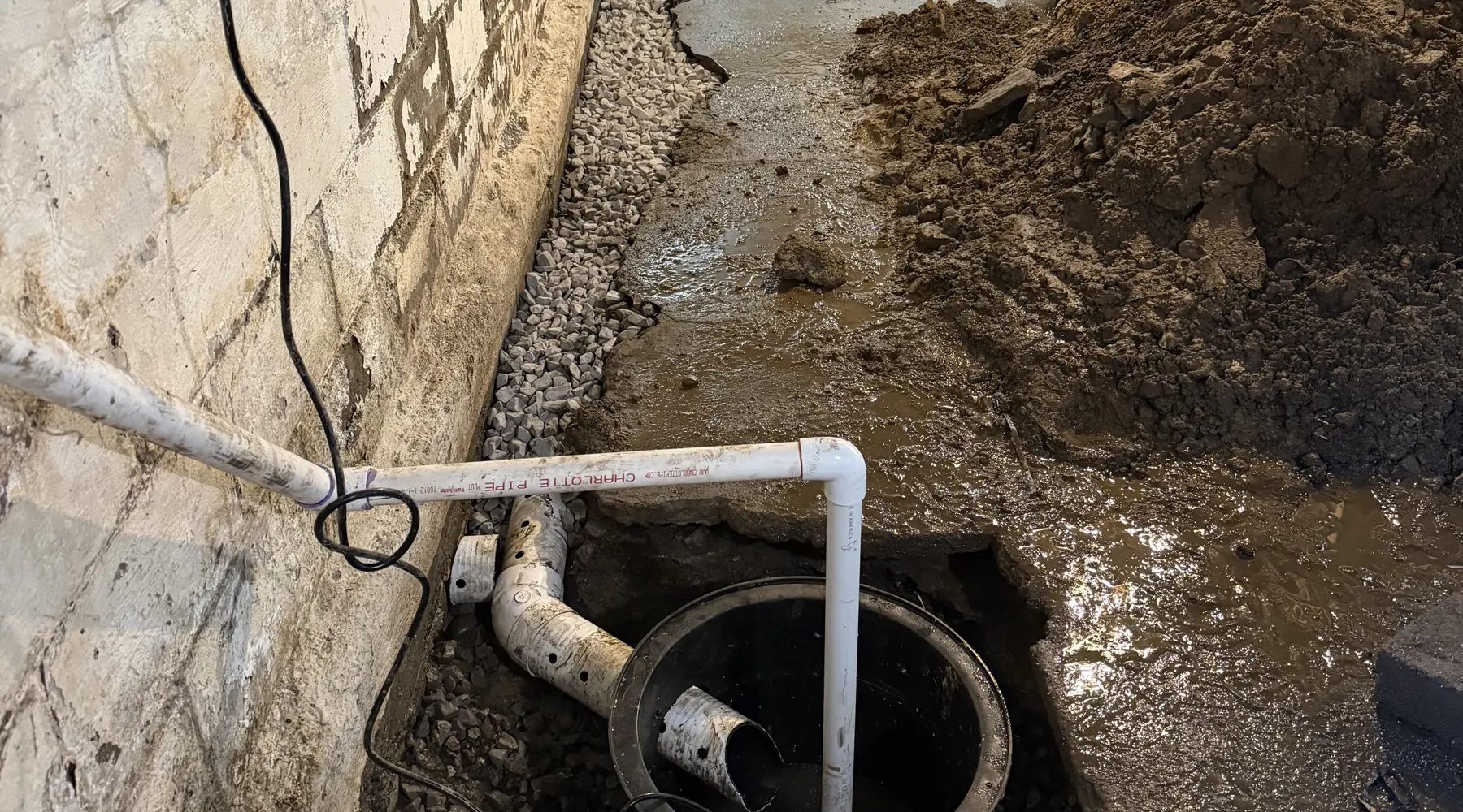 Interior perimeter trench with perforated pipe bedded in washed stone, running to a sump basin at the low point
