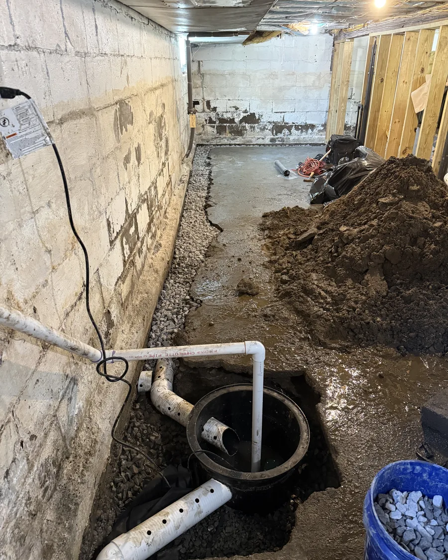 Perforated drainage pipe bedded in washed stone in an interior perimeter trench, running to an open sump basin