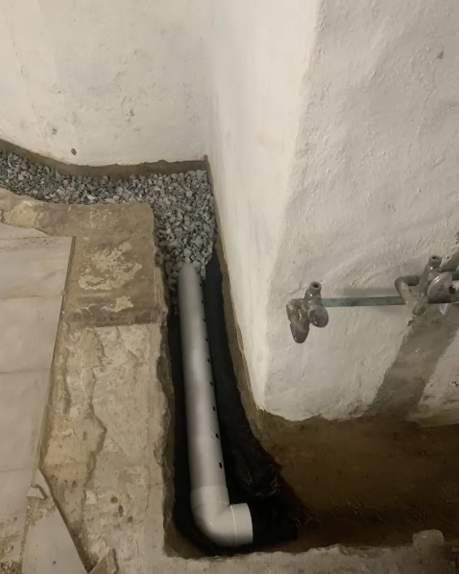 Perforated drainage pipe on filter fabric, bedded in washed stone beside a stone foundation