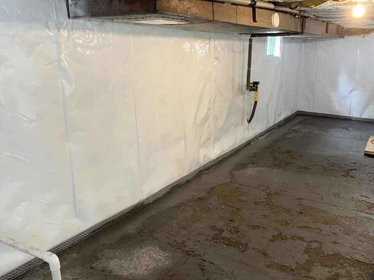 Finished basement with a white wall vapor barrier and a sealed sump basin lid in the floor