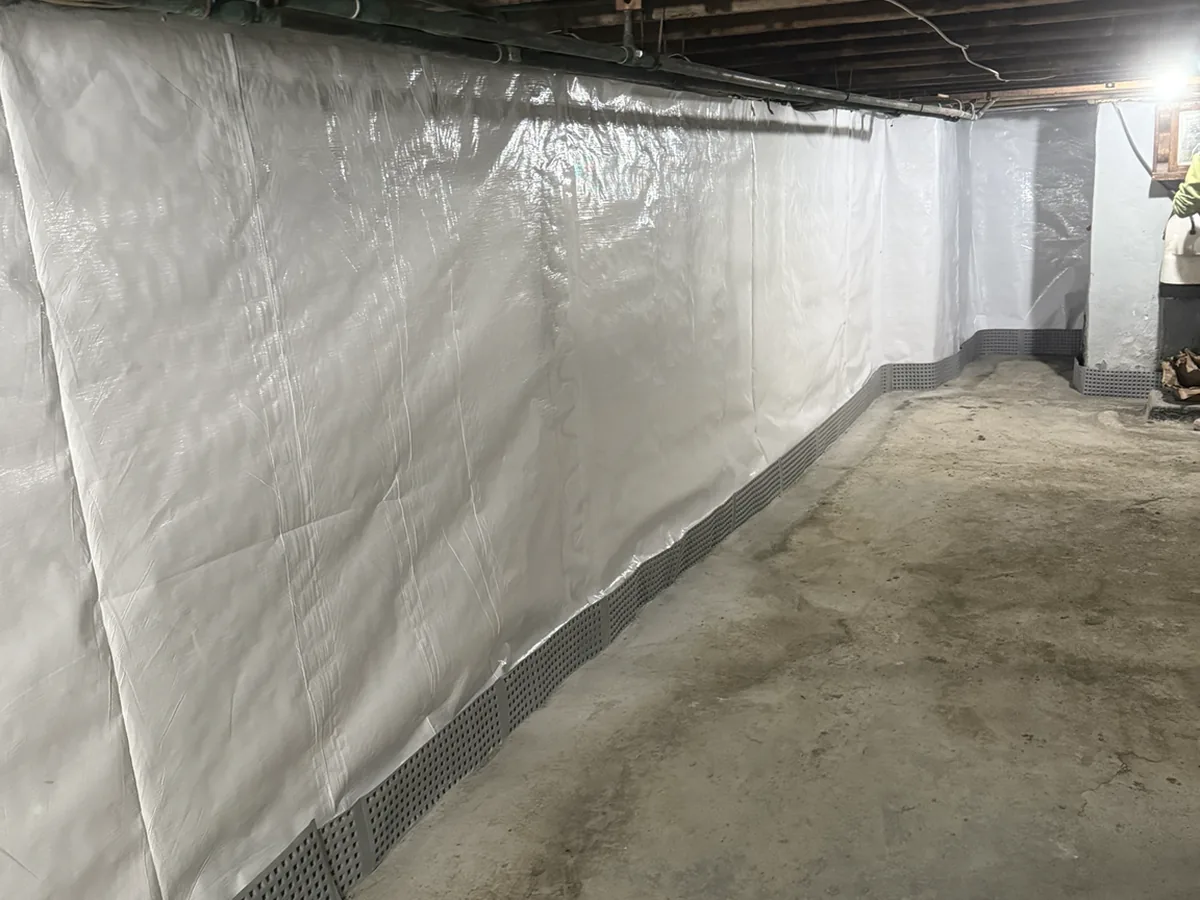 Long basement wall fully lined with a vapor barrier terminating into the perimeter drainage track